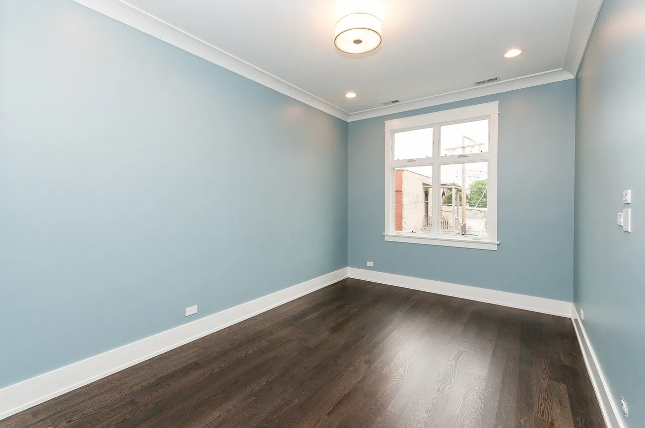 Empty bedroom painted soft blue with a single window overlooking the neighborhood.