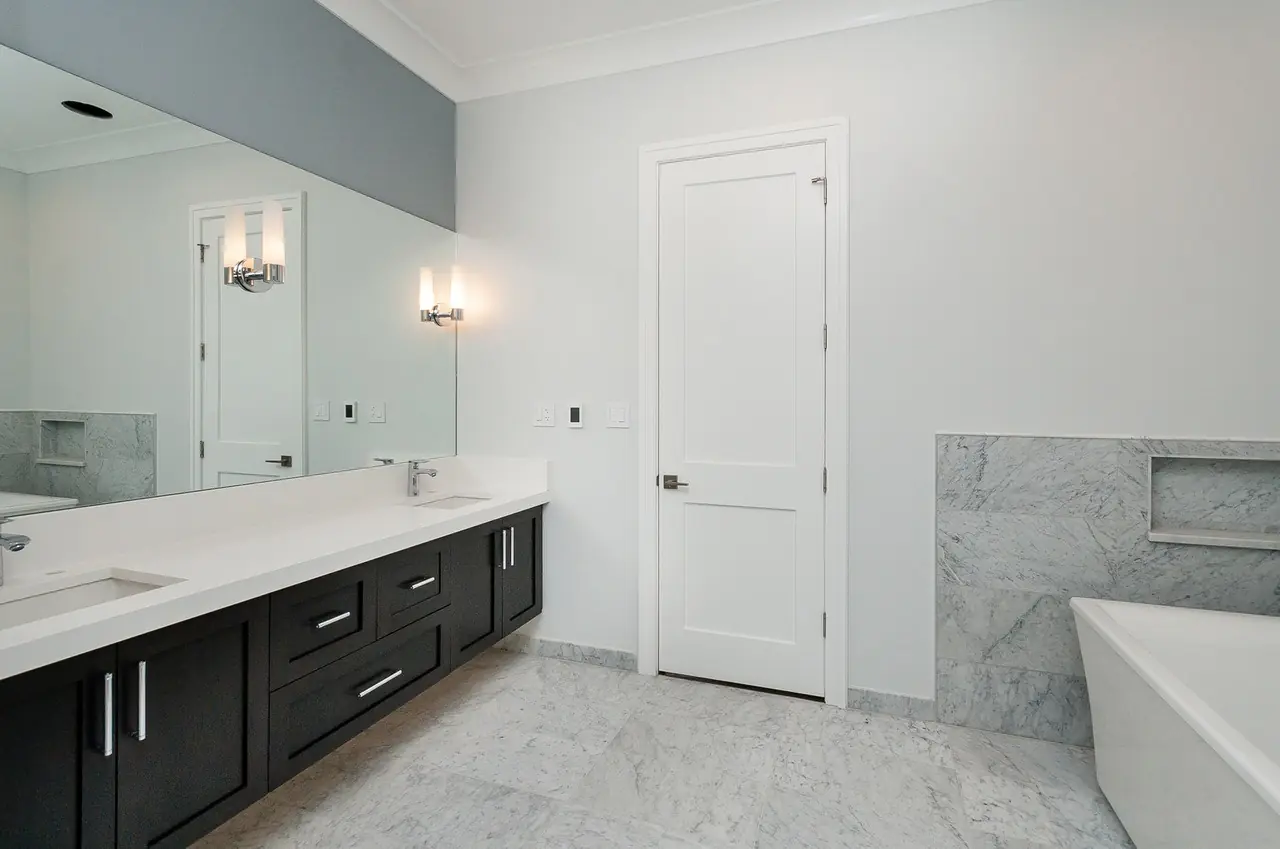 Second bathroom with a dark double vanity, marble flooring, and a soaking tub.