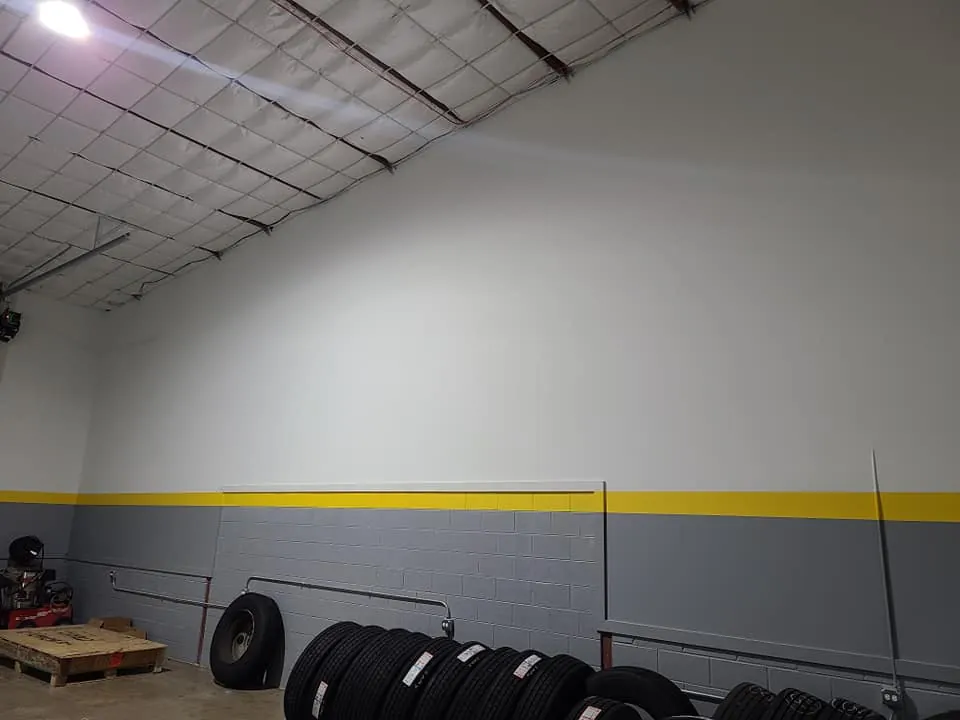 Warehouse addition interior wall with painted concrete block base, yellow safety stripe, and exposed insulated ceiling panels.