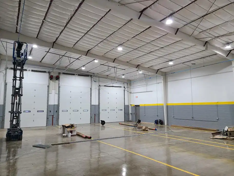 Interior of the new warehouse bay showing insulated metal roof decking, three overhead doors, and a freshly sealed concrete floor.