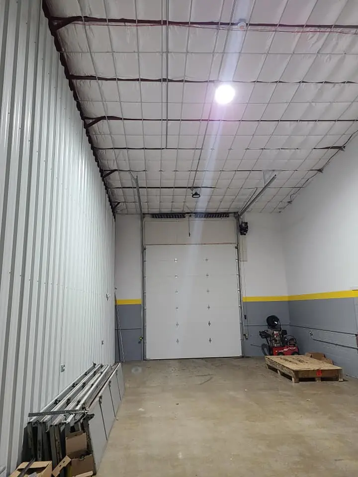 Newly framed warehouse bay with a single overhead door, exposed roof insulation, and unfinished concrete flooring.