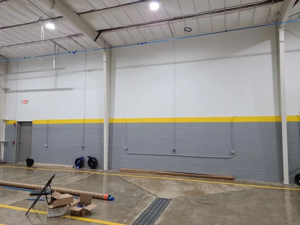 Block masonry wall inside the warehouse addition with a yellow accent band, exit door, and surface-mounted conduit runs.