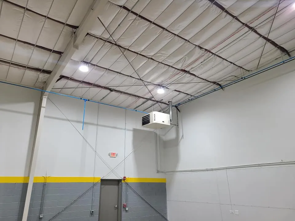 Suspended gas unit heater and exit signage installed beneath the exposed steel roof trusses of the warehouse addition.