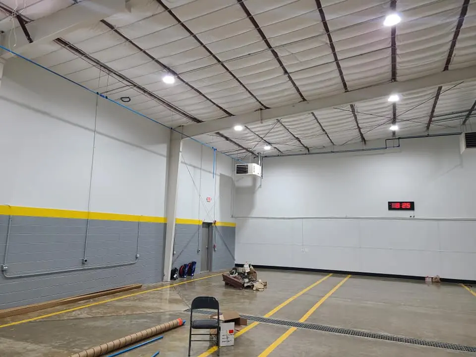 Open warehouse floor with exposed roof trusses, a wall-mounted unit heater, and a floor drainage channel.
