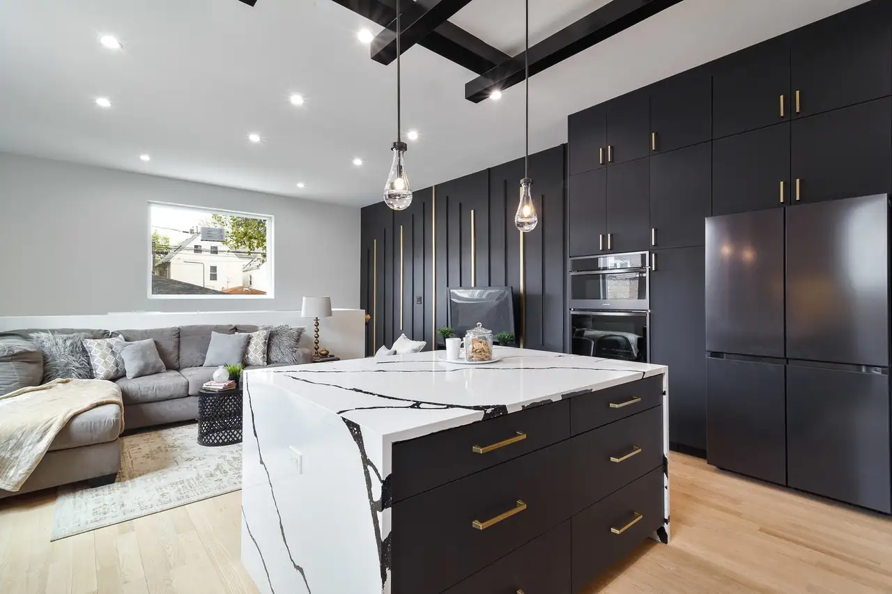 Open kitchen and living area with full-height black cabinetry, an integrated paneled fridge wall, and a marble waterfall island.
