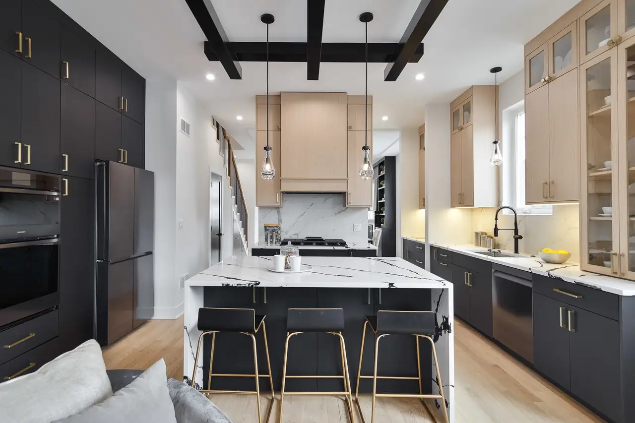 Kitchen with black lower cabinets, light oak uppers, a waterfall marble island, and black ceiling beams with glass pendant lights.