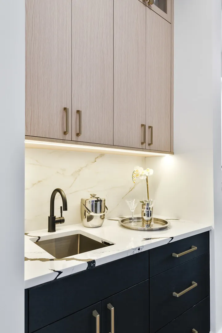Butler's pantry wet bar with a matte black faucet, marble waterfall counter, and glassware staged for entertaining.