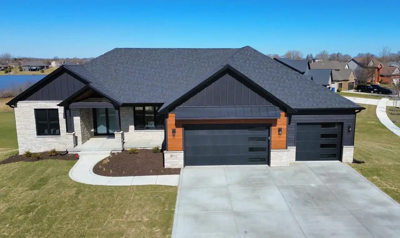 Aerial front view of the Lakeview New Construction home, showing its dark stone-and-wood facade and three-car garage.