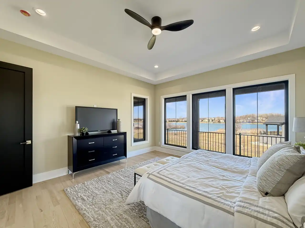 Primary bedroom with a wall of windows overlooking the lake and a dark wood media dresser.