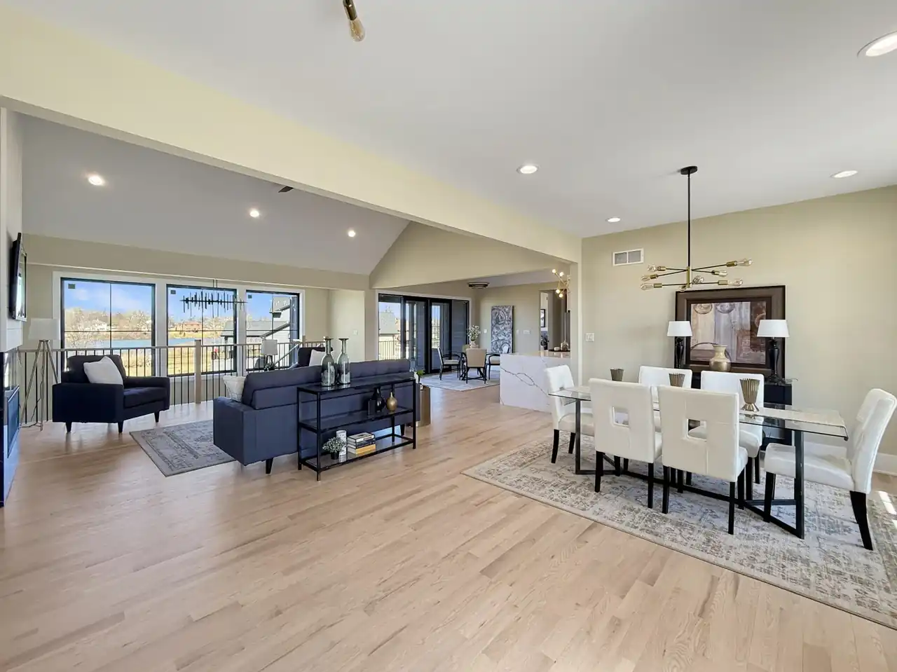 Open-concept living and dining area anchored by a glass dining table and modern linear chandelier.