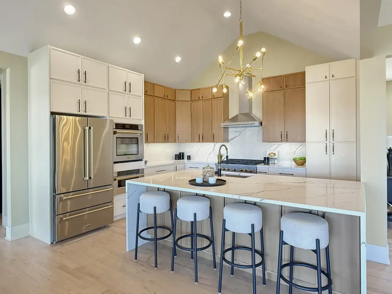 Kitchen with a quartz waterfall island, mixed wood-and-white cabinetry, and a brass starburst chandelier.