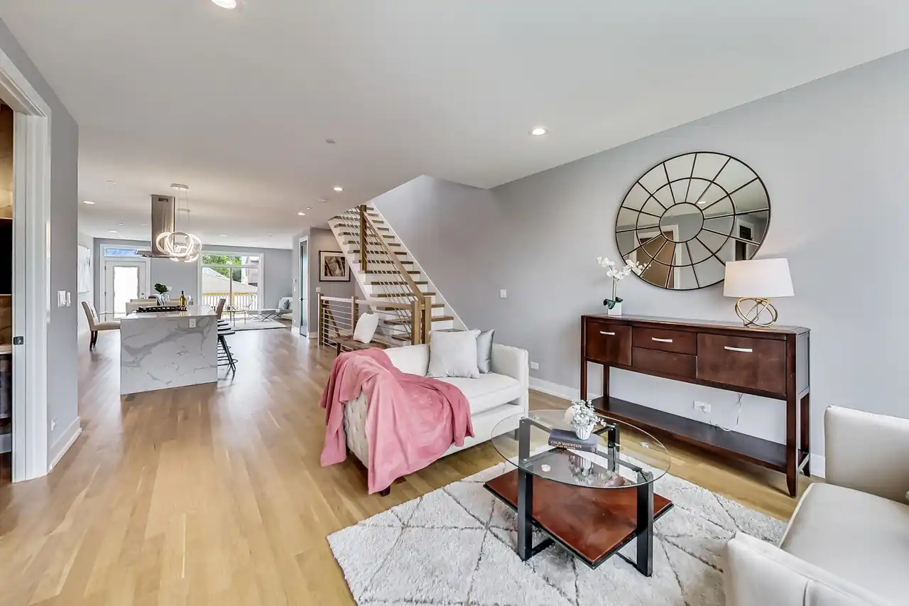 Open-concept living area with a wood and cable stair rail, marble waterfall kitchen island visible beyond.