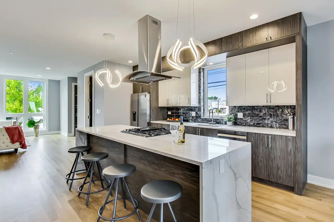 Wide kitchen view with a matte black hood, marble slab backsplash, bar seating for four, and stainless refrigerator.
