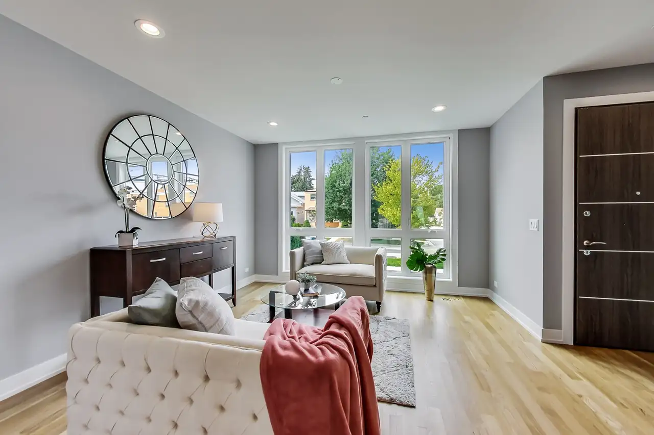 Staged living room with a round sunburst mirror, tufted sofa, and a wall of windows facing the front yard.