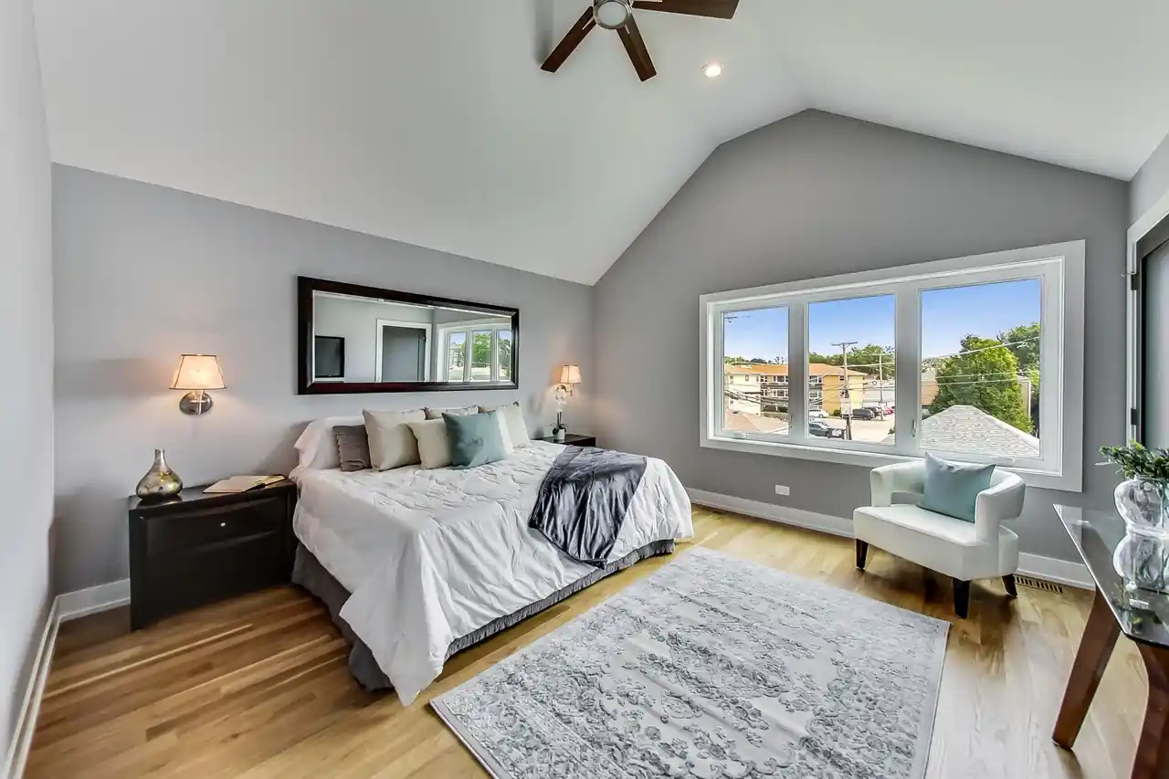 Primary bedroom with a vaulted ceiling, ceiling fan, and a bank of windows overlooking the street.