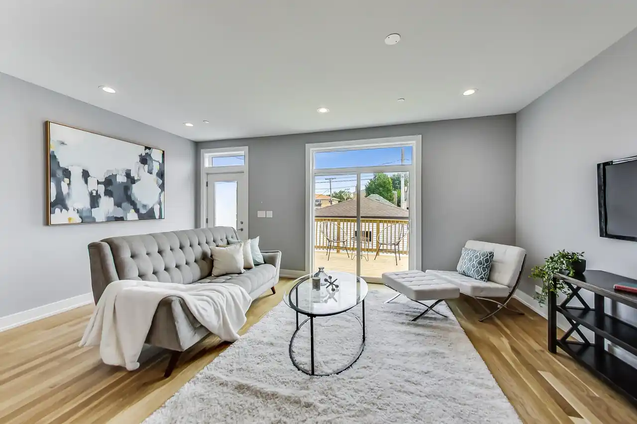 Family room with a tufted gray sofa, round glass coffee table, and sliding door opening to the back deck.