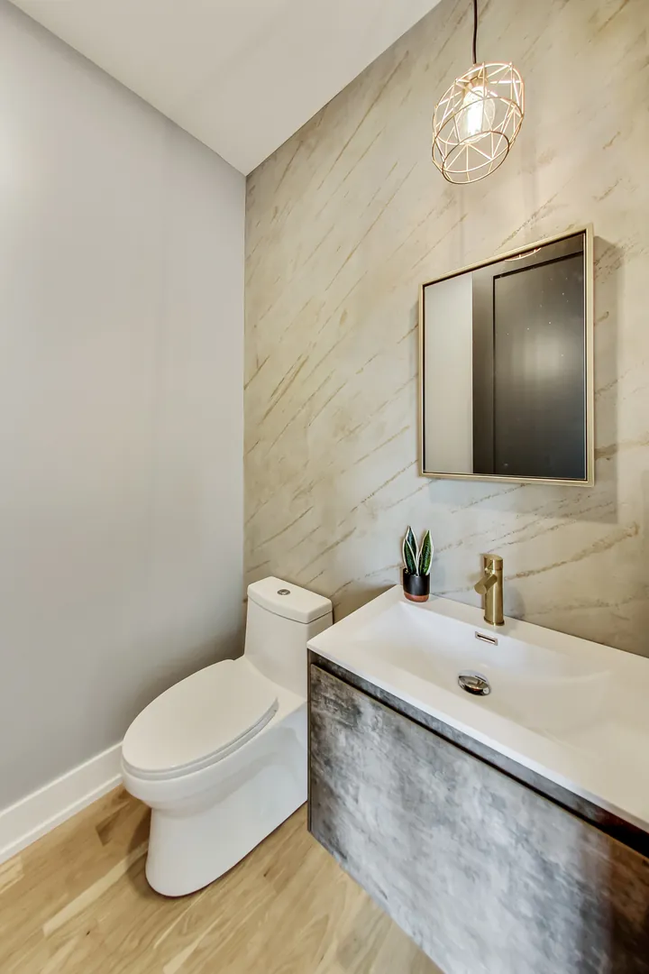 Powder room with a wall-mounted vanity, brass faucet, and a wavy stone-look accent wall.