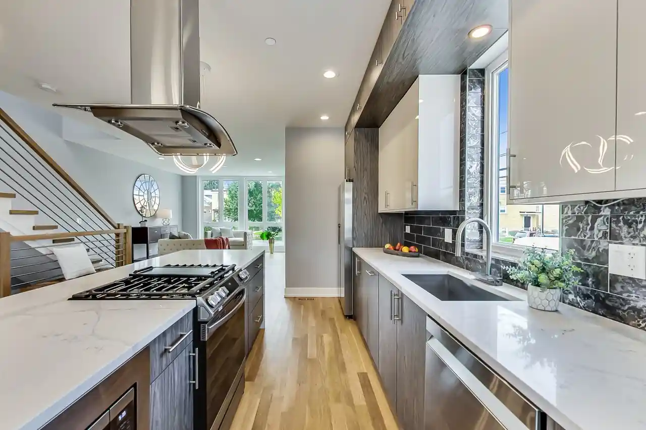 Galley-style kitchen with a gas range, marble subway tile backsplash, and sightline down the hall to the stairs.