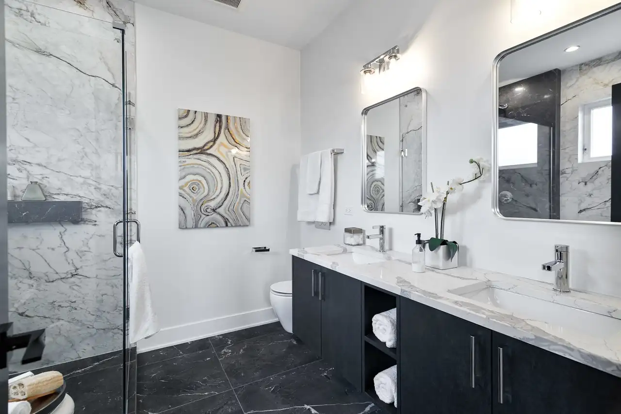 Primary bathroom with a marble-slab shower, dark floating vanity, dual sinks, and individual framed mirrors.