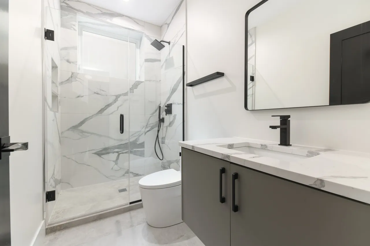 Bathroom with a frameless glass shower, book-matched marble slab walls, and a dark green vanity.