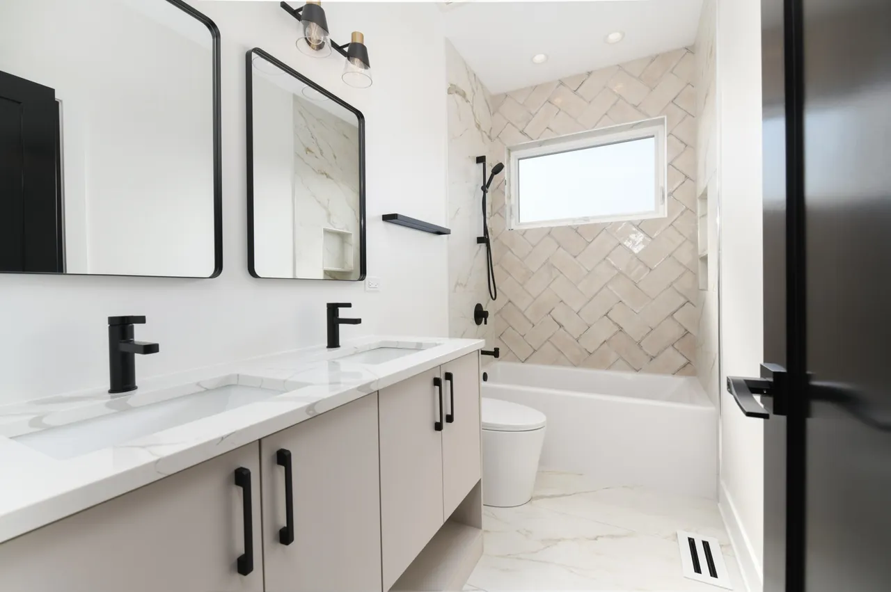 Guest bathroom with herringbone tile in the tub surround, matte black fixtures, and a black-framed double vanity.