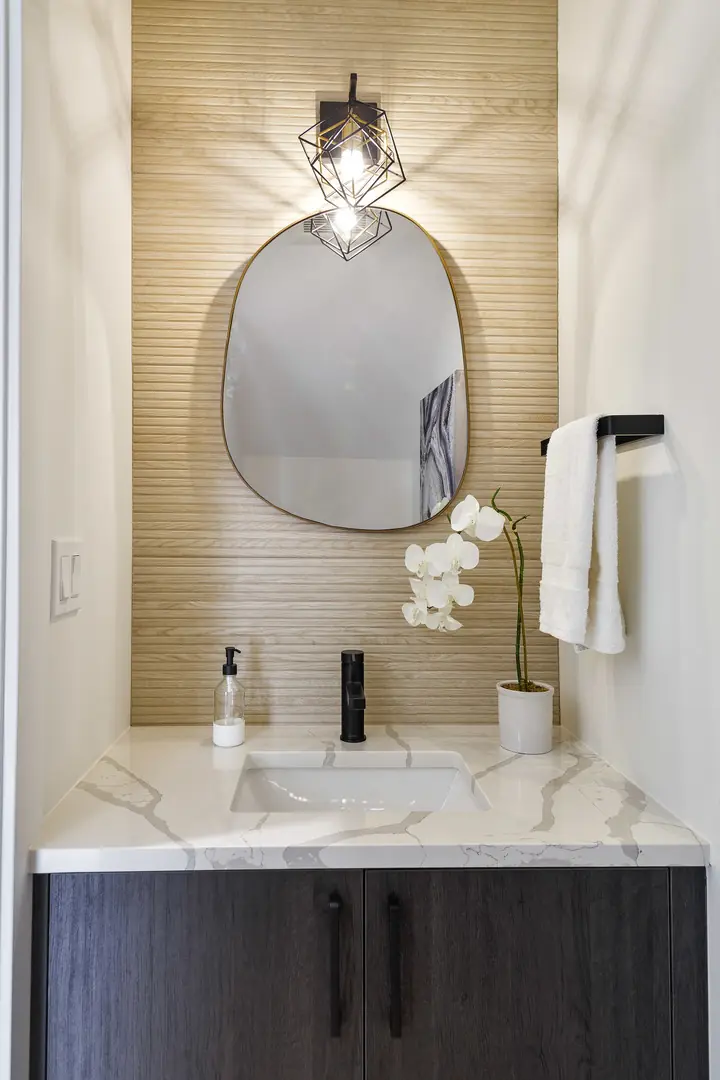 Powder room with an organic-shaped mirror, geometric wall sconce, wood-slat accent wall, and marble vanity top.
