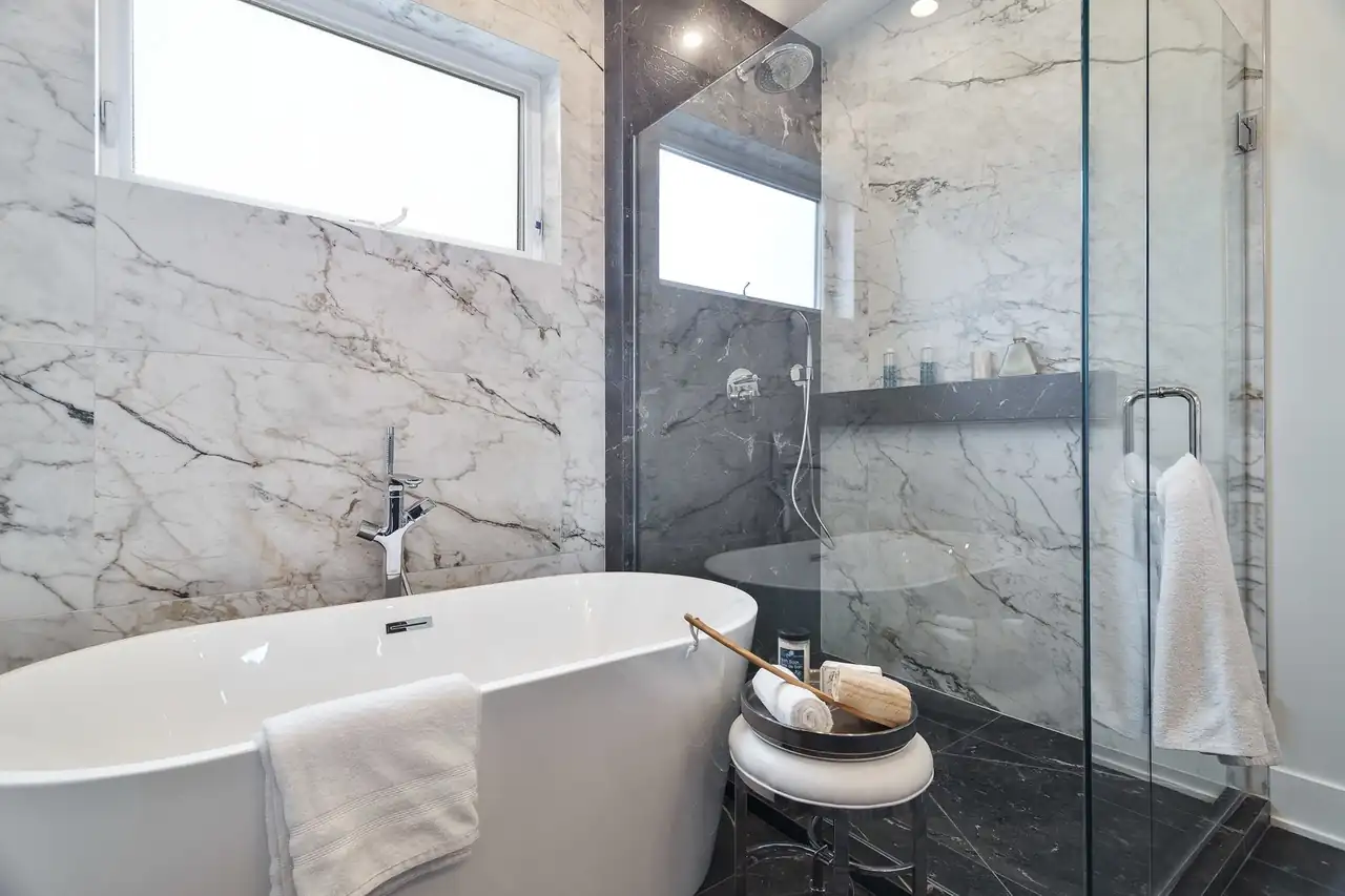 Spa-style bathroom with a freestanding soaking tub, marble walls, and a glass-enclosed rain shower.