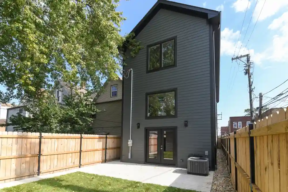 Rear exterior of the Kimball New Construction home showing charcoal siding, a stone patio, and wood privacy fencing.