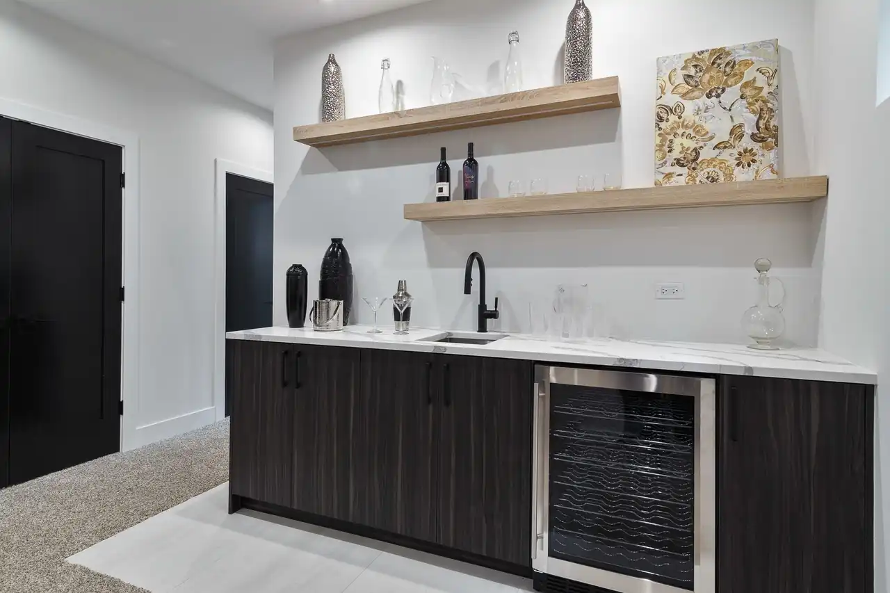 Basement wet bar with floating wood shelves, a wine fridge, and a matte black faucet over a marble counter.