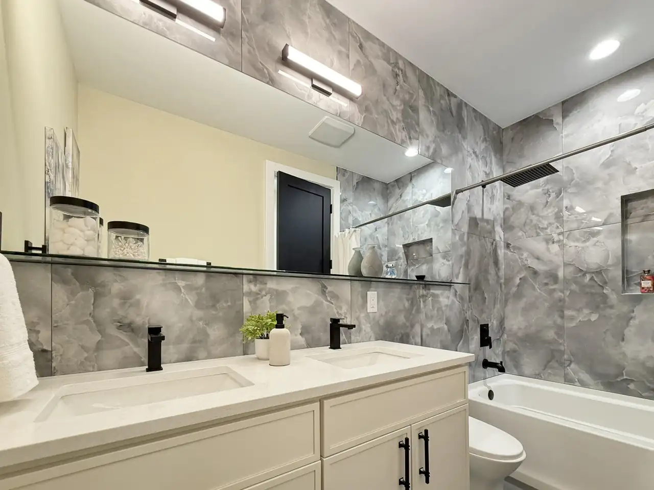 Full bathroom with a marble-look tiled tub-shower combo and a white double-sink vanity.