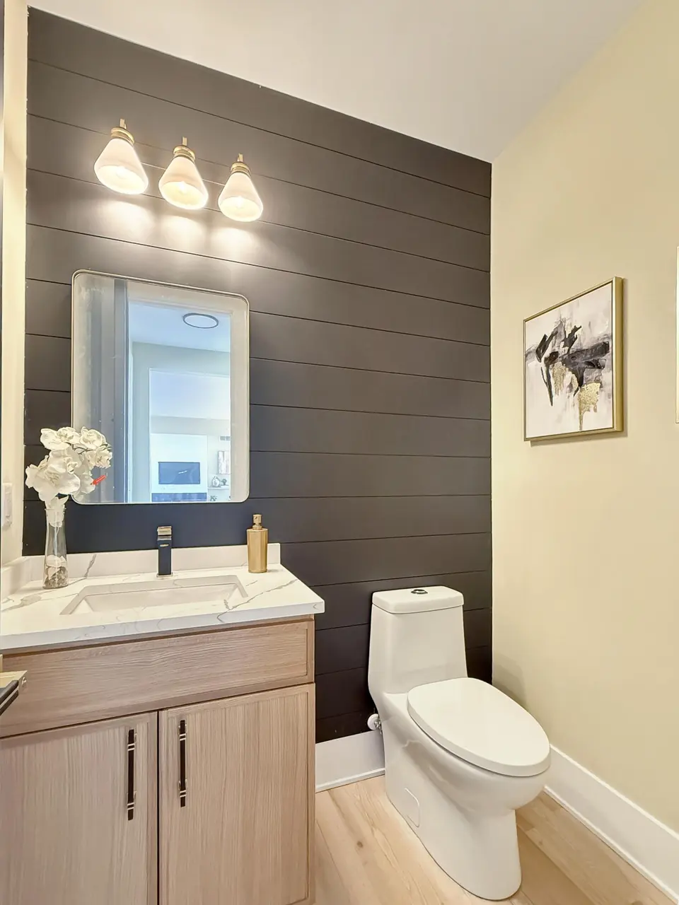 Powder room with a dark shiplap accent wall behind the toilet and a light wood floating vanity.
