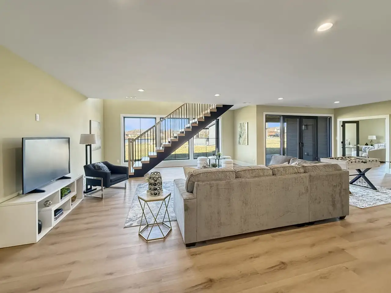 Lower-level rec room with an open staircase, sectional seating, and a foosball table.