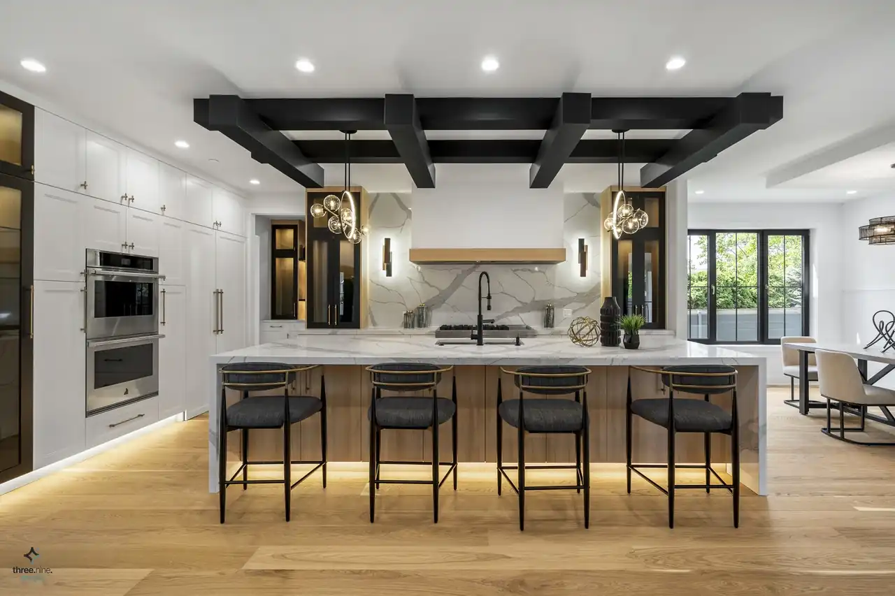 Kitchen island with waterfall marble countertop beneath a black coffered beam ceiling