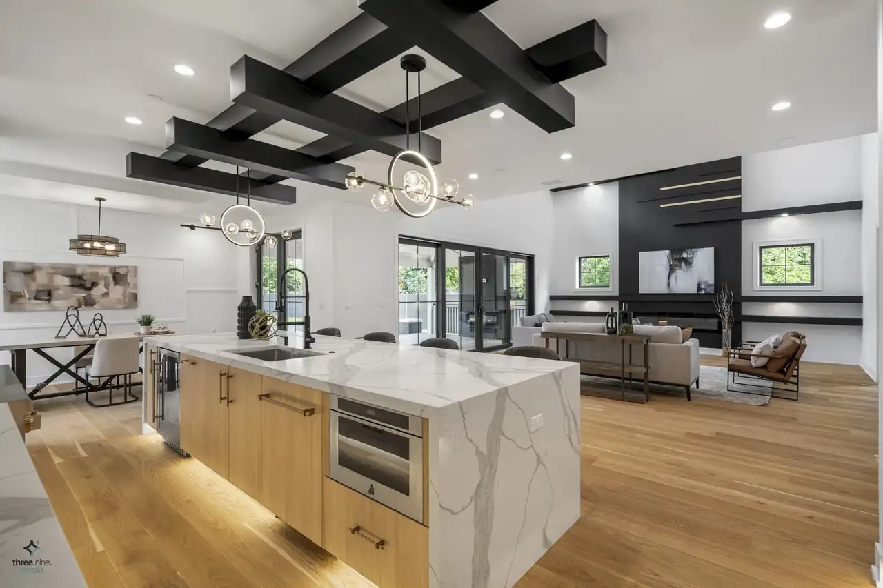 Kitchen island opens to the dining and living areas under a crossed black beam ceiling
