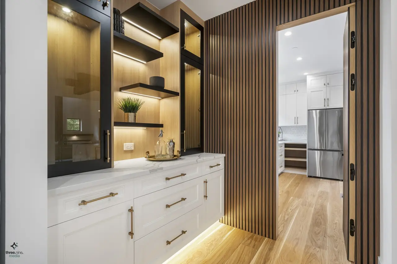Butler's pantry with glass-front cabinets, lit wood shelving, and a wood slat accent wall
