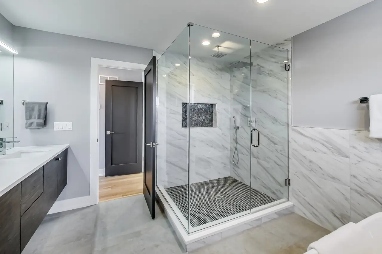 Frameless glass shower finished in marble-look tile with a rain shower head and built-in niche.