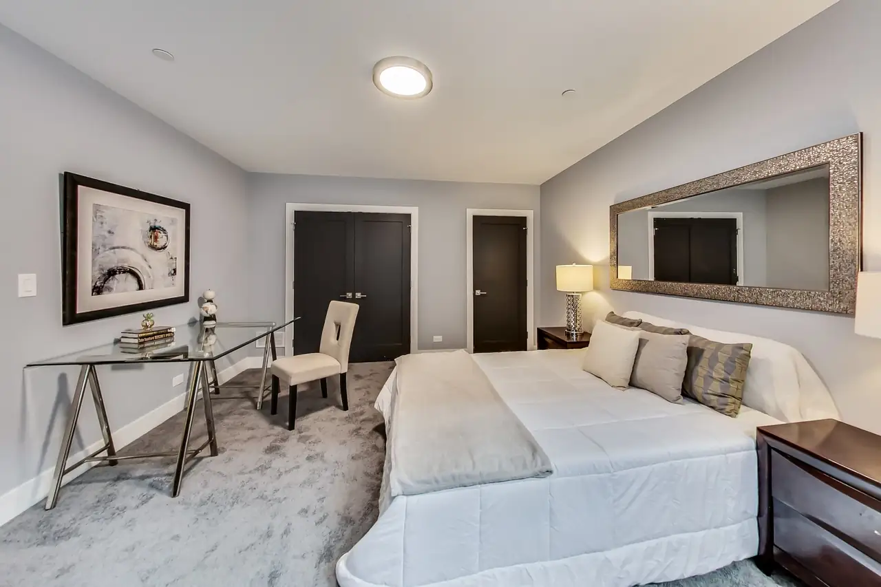 Lower-level bedroom with a glass desk, dark closet doors, and a mirrored headboard wall.