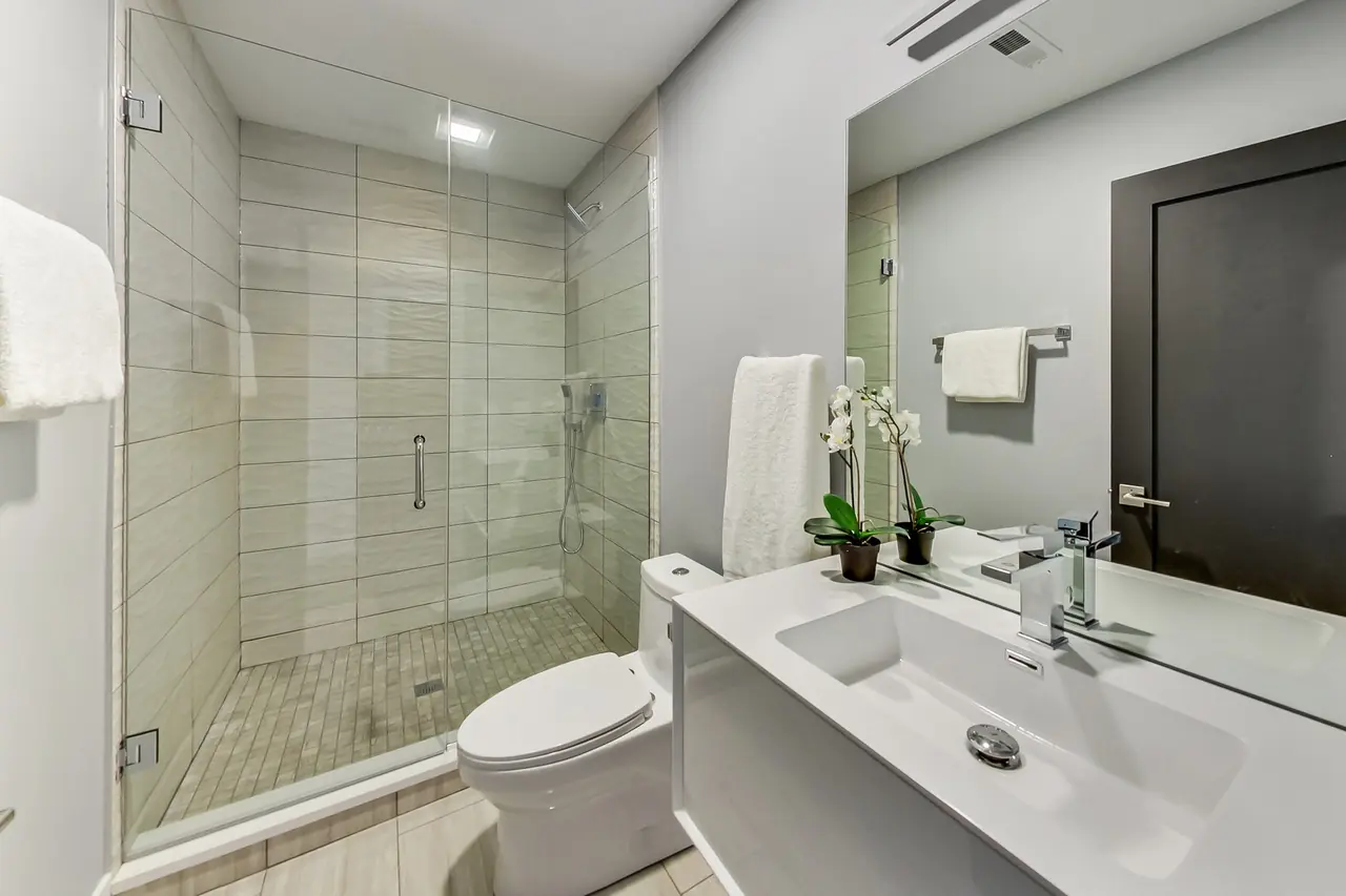Bathroom with a tiled walk-in shower, single vanity, and potted orchids on the counter.