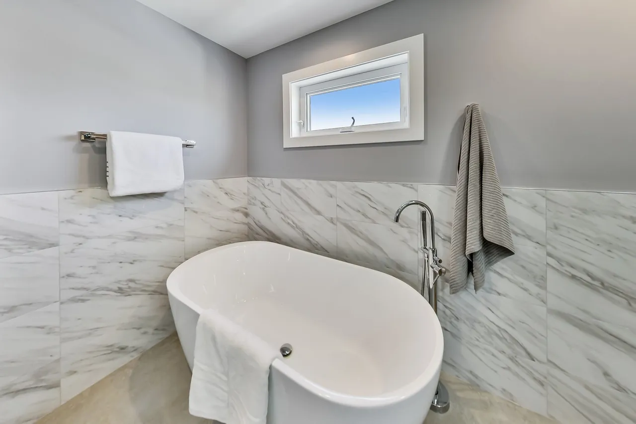 Freestanding soaking tub set against marble tile wainscoting with a floor-mounted filler.