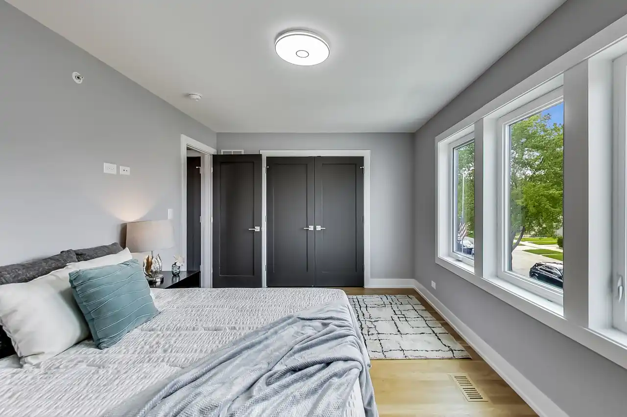 Secondary bedroom with dark double closet doors and three windows overlooking the front yard.