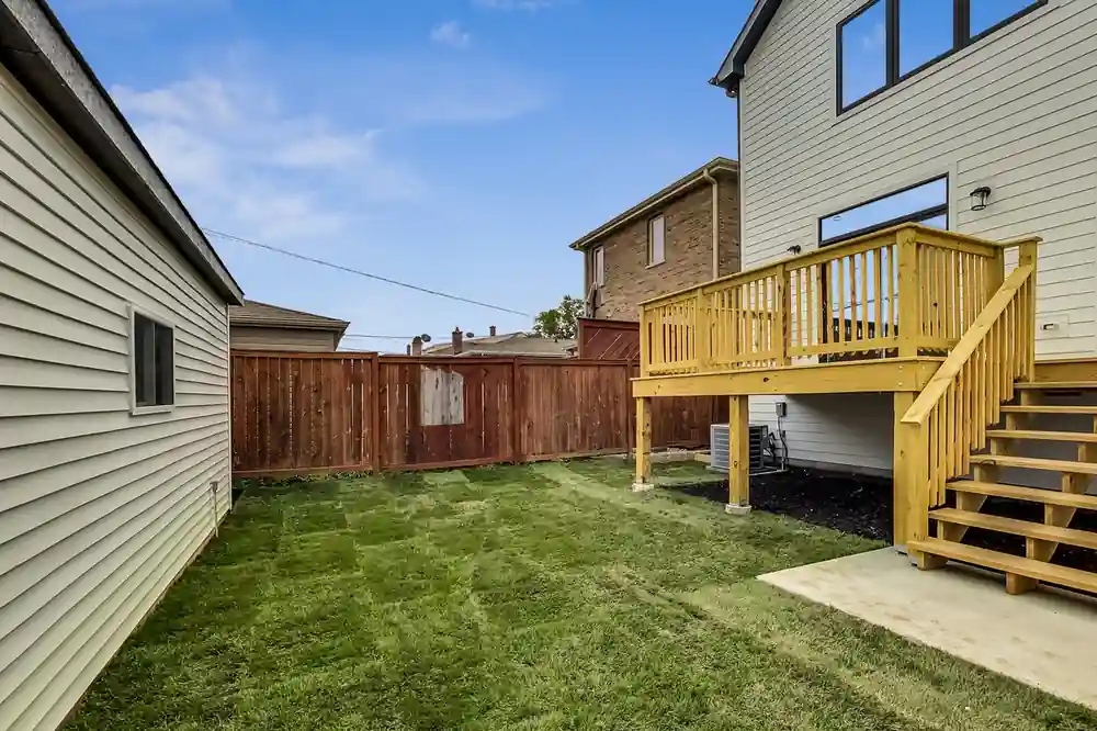 Fenced backyard with a fresh lawn, wood privacy fencing, and the elevated back deck above.