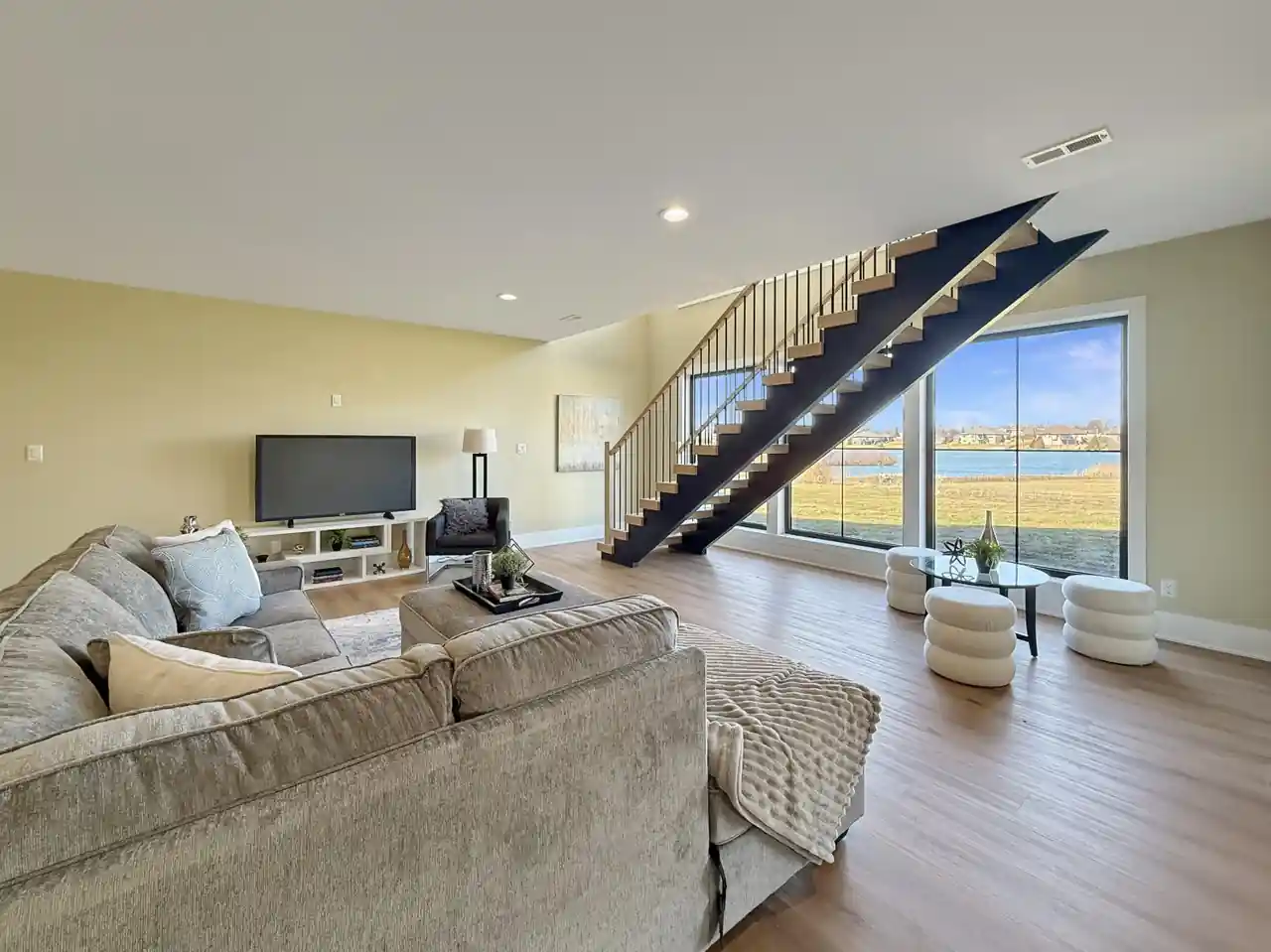 Family room with a plush sectional sofa, floating staircase, and wide lake-view windows.
