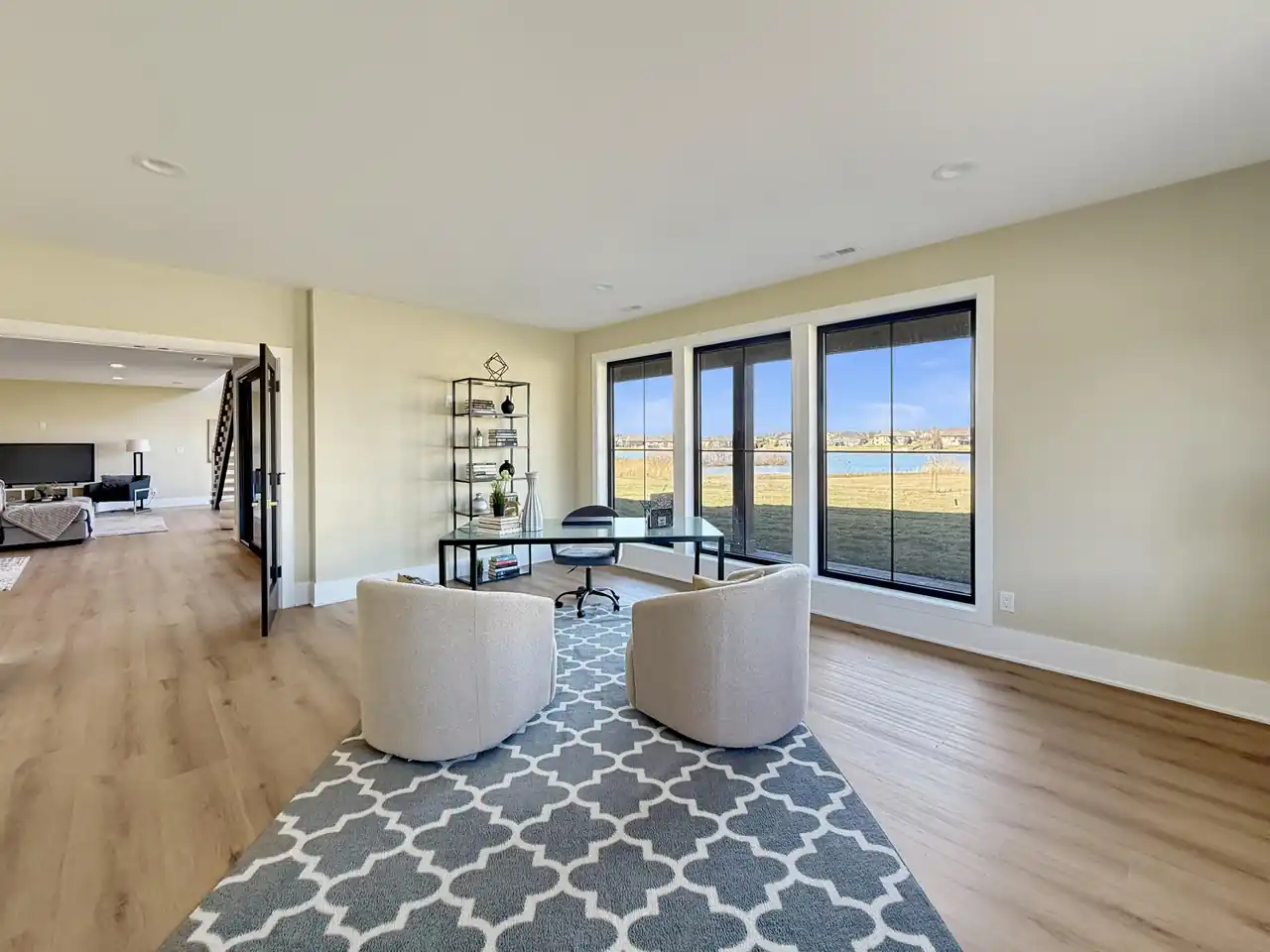 Home office with a glass desk, boucle accent chairs, and three tall windows facing the lake.