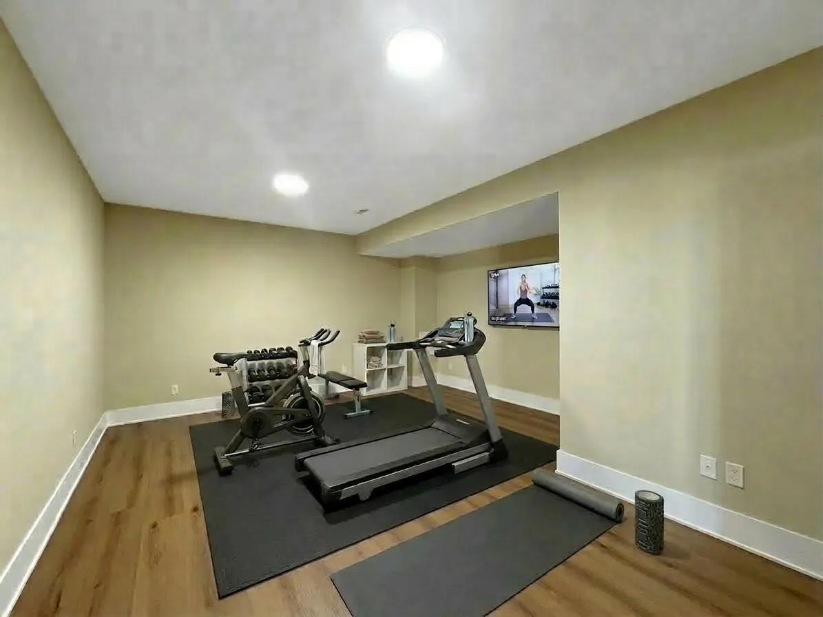 Home gym outfitted with a treadmill, stationary bike, and a wall-mounted workout display.