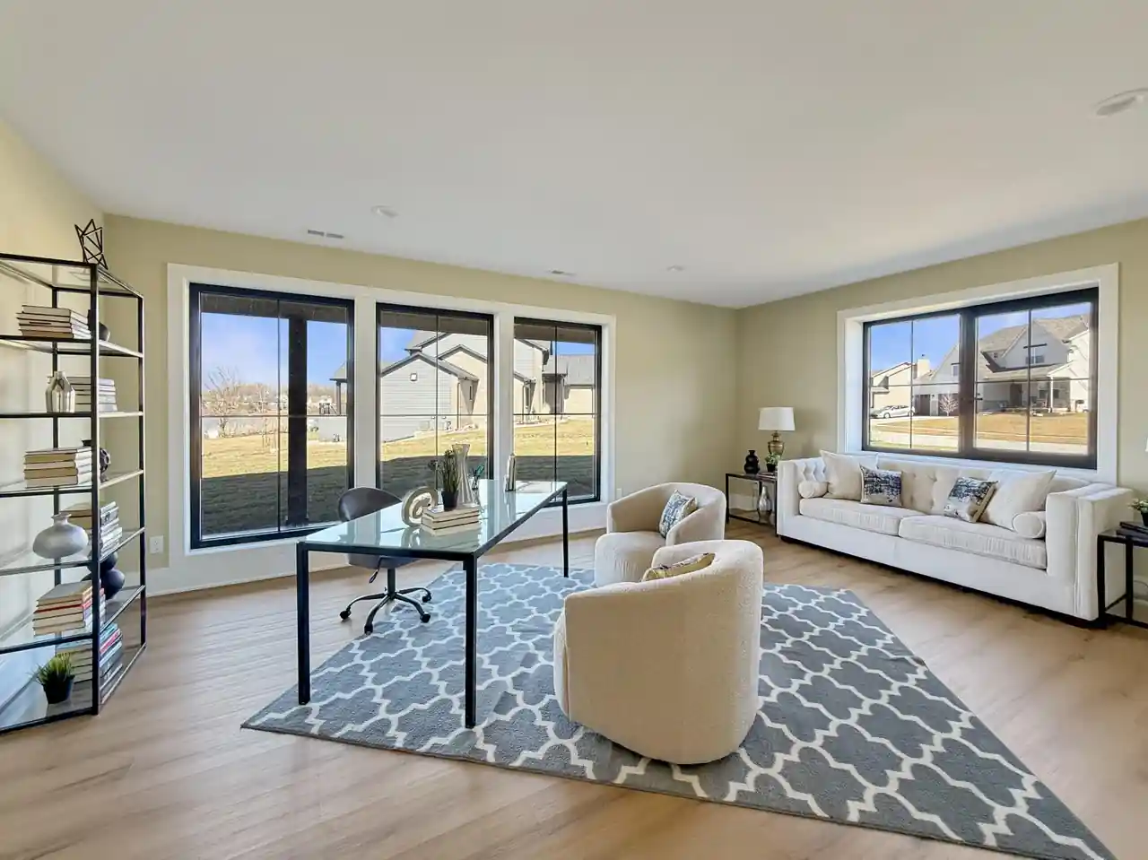 Flex room with a glass desk, ladder bookshelf, and a tufted sofa near oversized windows.