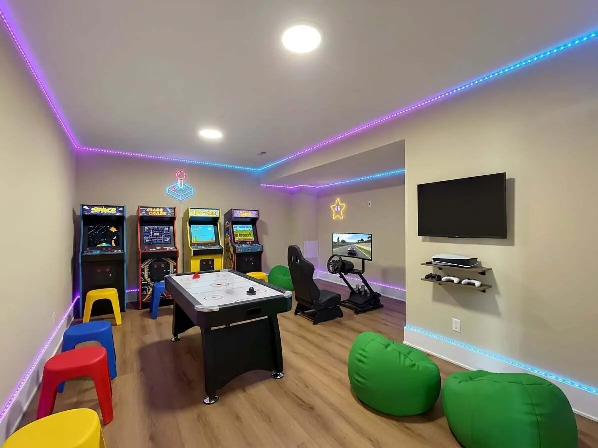 Arcade and game room featuring an air hockey table, racing simulator, and neon accent lighting.