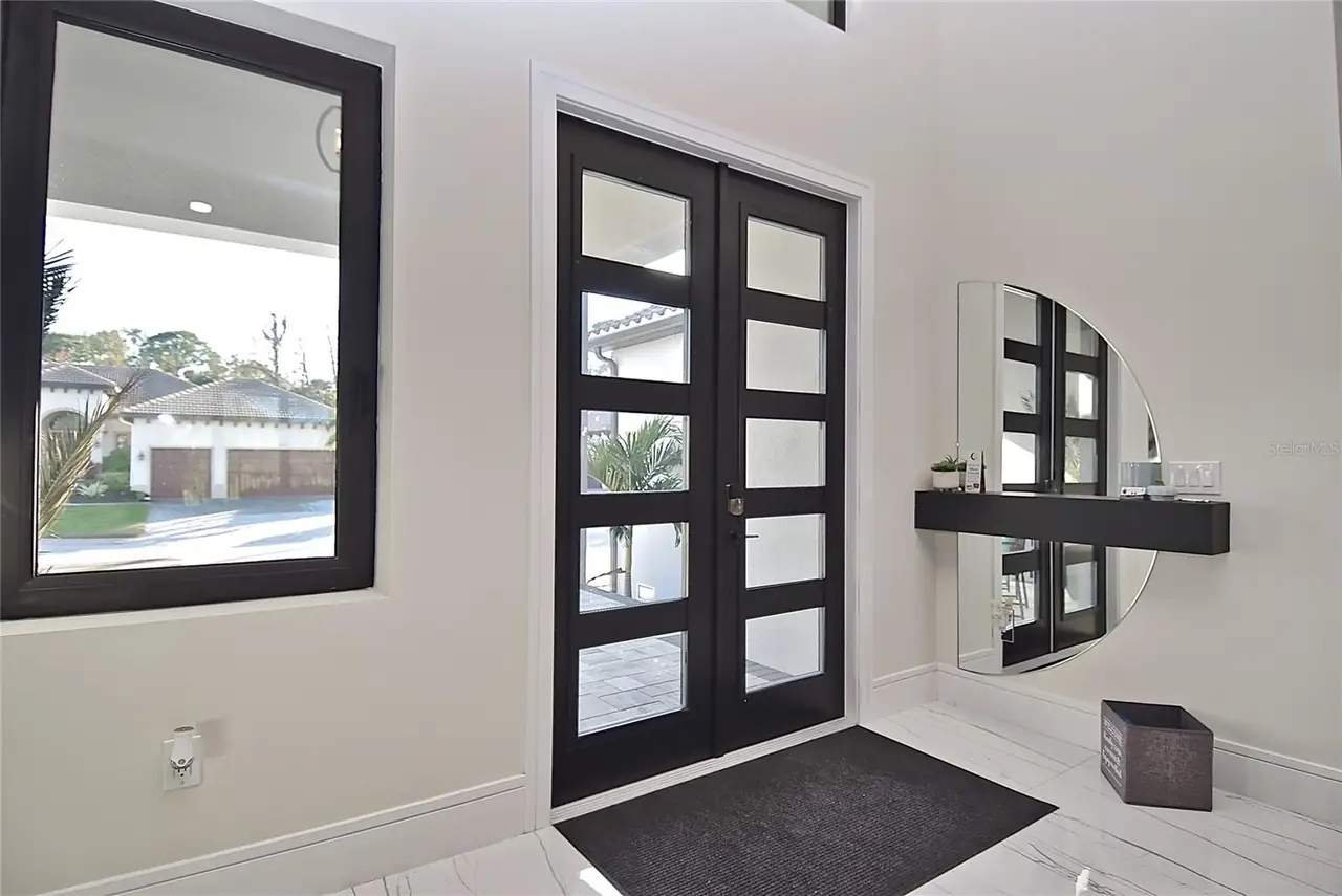 Foyer with dark-framed glass entry doors, a round wall mirror, and marble-look tile flooring.