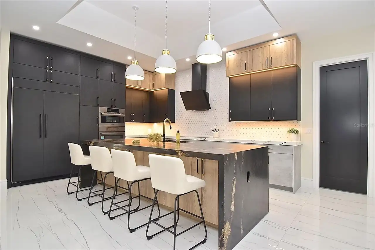 Kitchen with dark cabinetry, an integrated paneled refrigerator, and a wood-tone waterfall island.