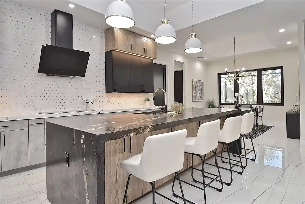 Kitchen island topped with waterfall marble, a black vent hood, and white pendant lighting.