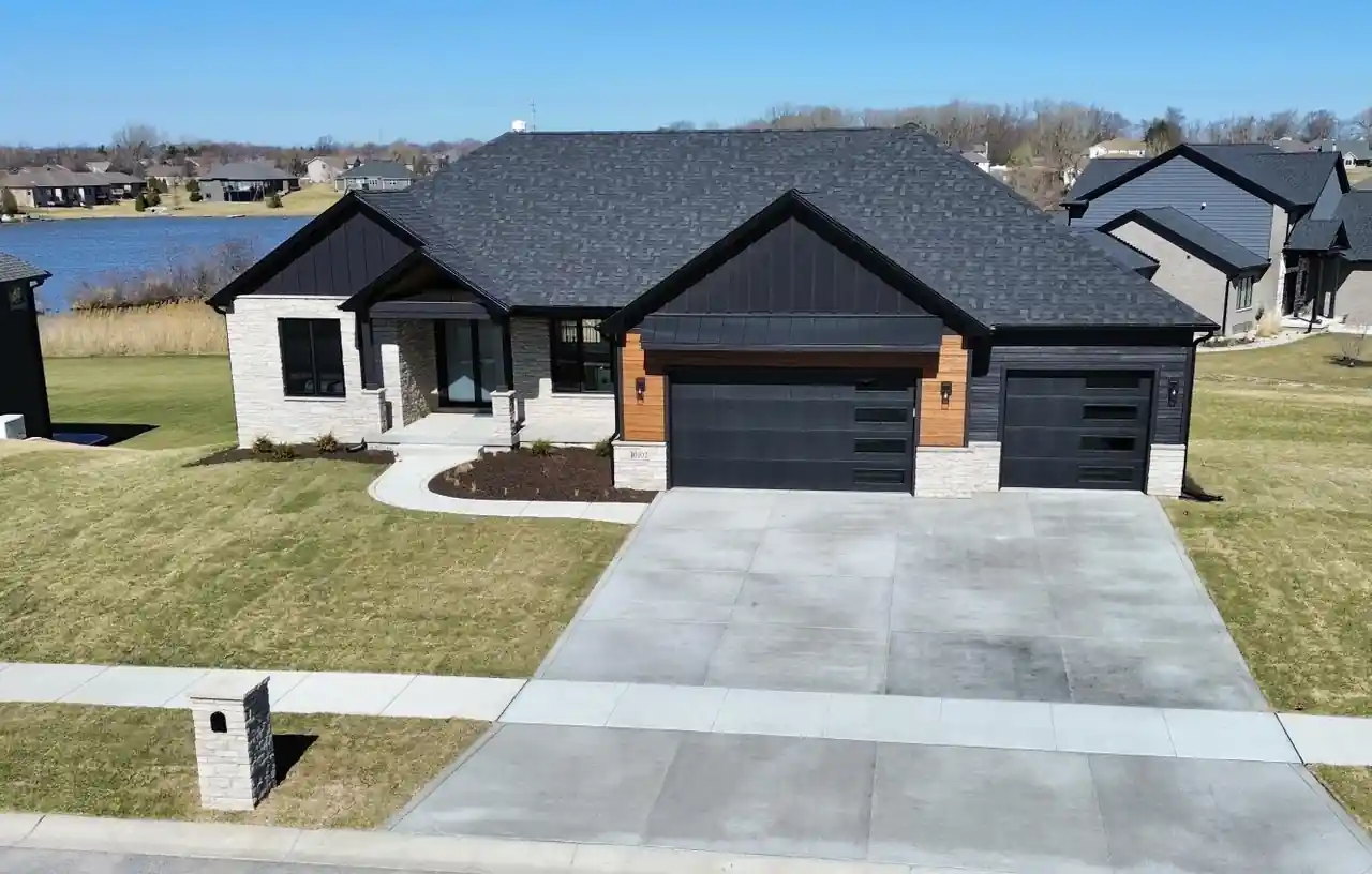 Angled aerial view of the home's stone-and-siding exterior with the lake visible beyond.